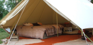 une tente ouverte lessant voir l'intérieur avec un grand lit deux places des tapis de sol